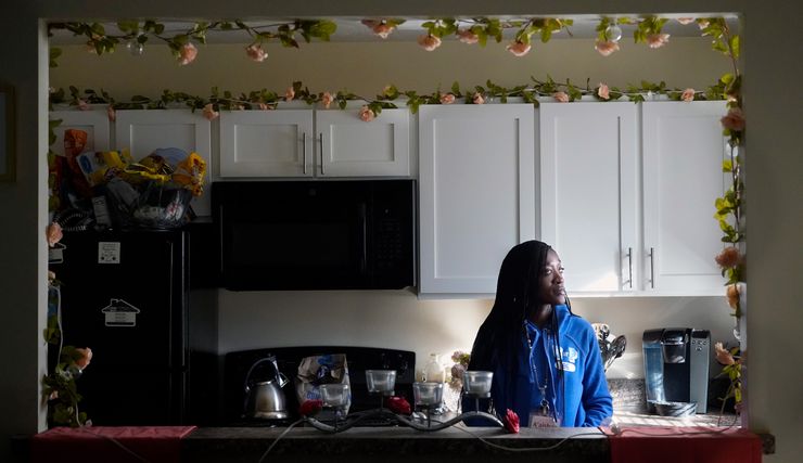 A Black woman in a blue shirt stands in a kitchen.